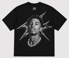 A black short-sleeve t-shirt featuring a large black-and-white graphic print of a man's portrait with a diamond chain necklace and a starburst design on the back. The number '10' is printed in white near the upper neckline. JUDE BELLINGHAM 