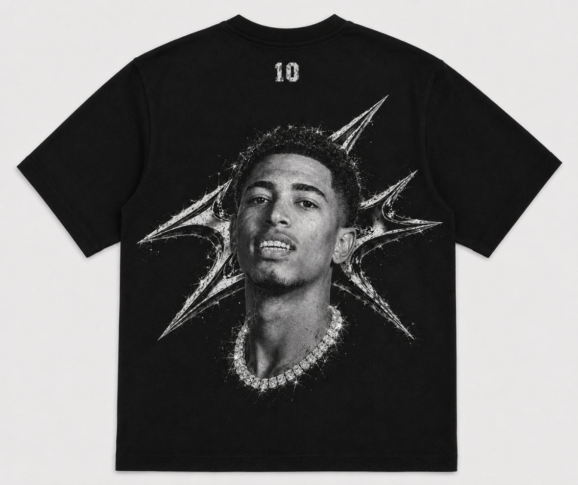 A black short-sleeve t-shirt featuring a large black-and-white graphic print of a man's portrait with a diamond chain necklace and a starburst design on the back. The number '10' is printed in white near the upper neckline. JUDE BELLINGHAM 