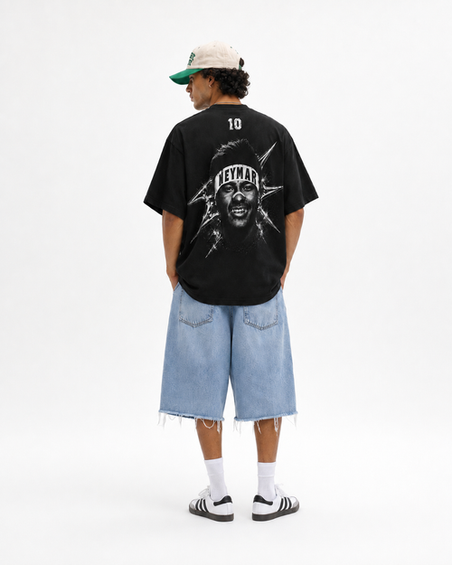 A model shown from the back wearing a black oversized t-shirt with a large graphic print of a face and the word 'NEYMAR' on the back, paired with light blue denim shorts, white socks, and black-and-white sneakers against a plain white background.