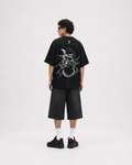 A model shown from the back wearing a black oversized t-shirt with a large white graphic print on the back, paired with black denim shorts, white socks, and black sneakers, set against a plain light gray studio background. ronaldo