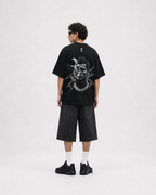 A model shown from the back wearing a black oversized t-shirt with a large white graphic print on the back, paired with black denim shorts, white socks, and black sneakers, set against a plain light gray studio background. ronaldo