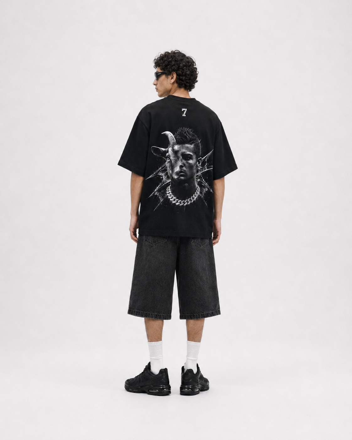 A model shown from the back wearing a black oversized t-shirt with a large white graphic print on the back, paired with black denim shorts, white socks, and black sneakers, set against a plain light gray studio background. ronaldo